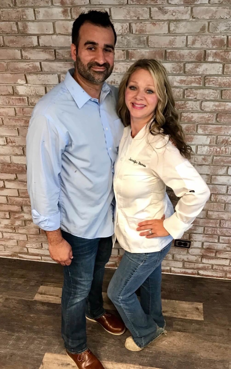 Jennifer and David, the owners, in front of the brick wall inside the bakery
